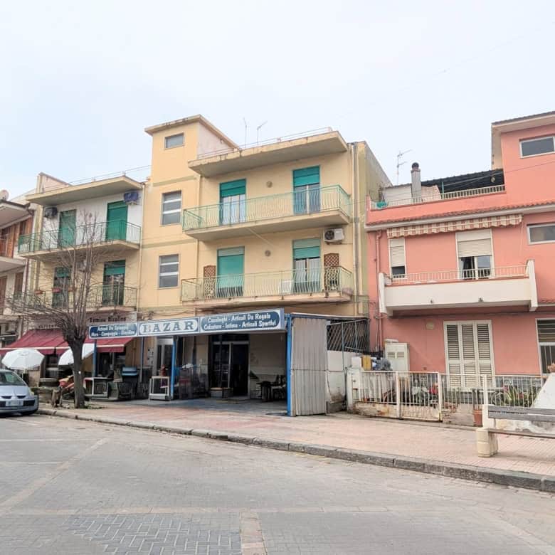 Edificio residenziale con negozio al piano terra, in una strada urbana, con auto parcheggiate e negozio di alimentari.