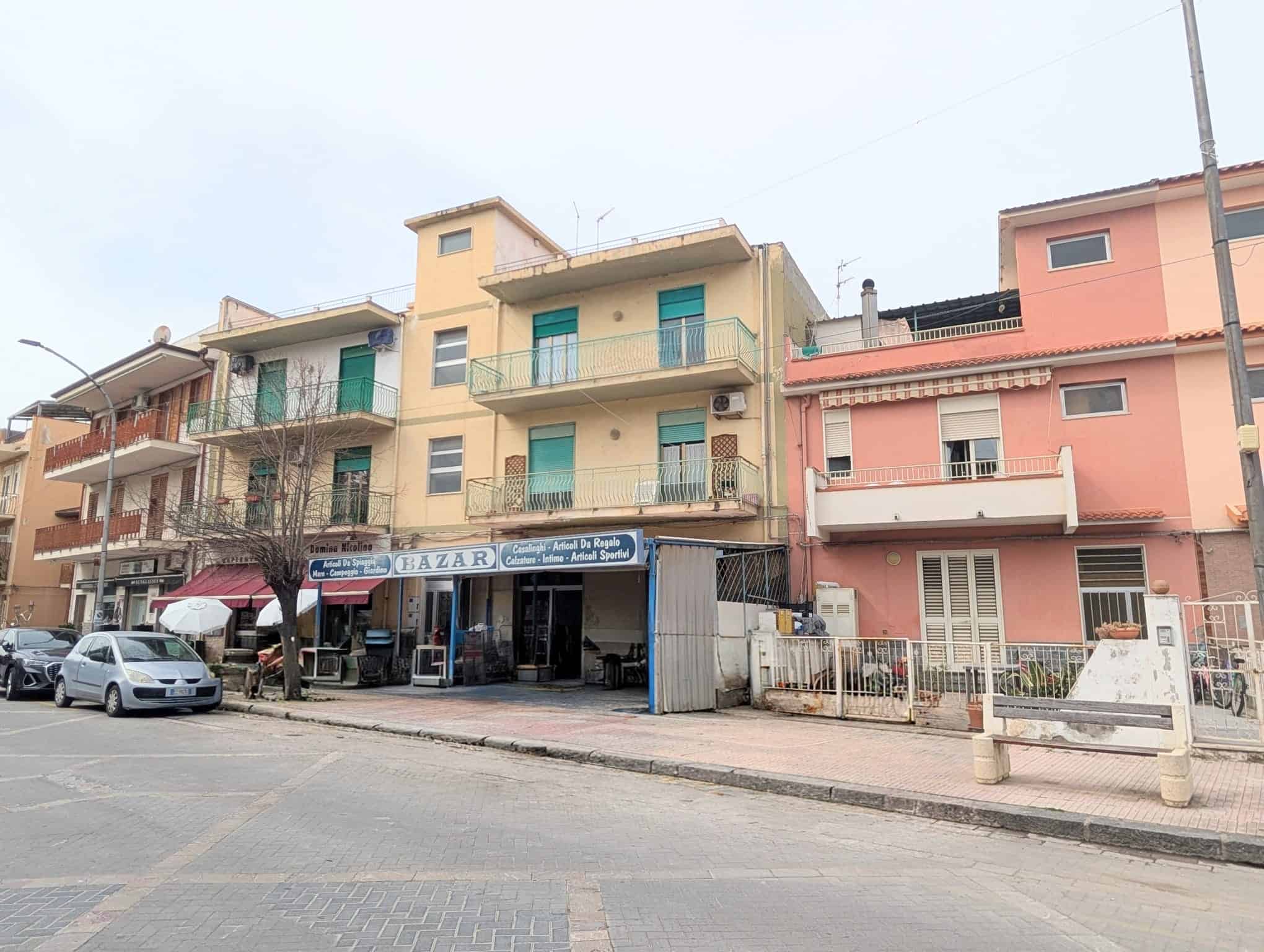 Edificio residenziale con negozio al piano terra, in una strada urbana, con auto parcheggiate e negozio di alimentari.