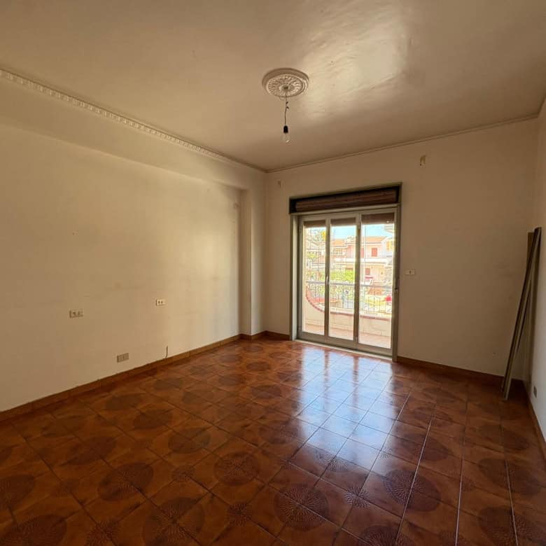 Interno di un appartamento vuoto con pareti bianche, pavimento in ceramica e grande finestra con balcone a Merì.