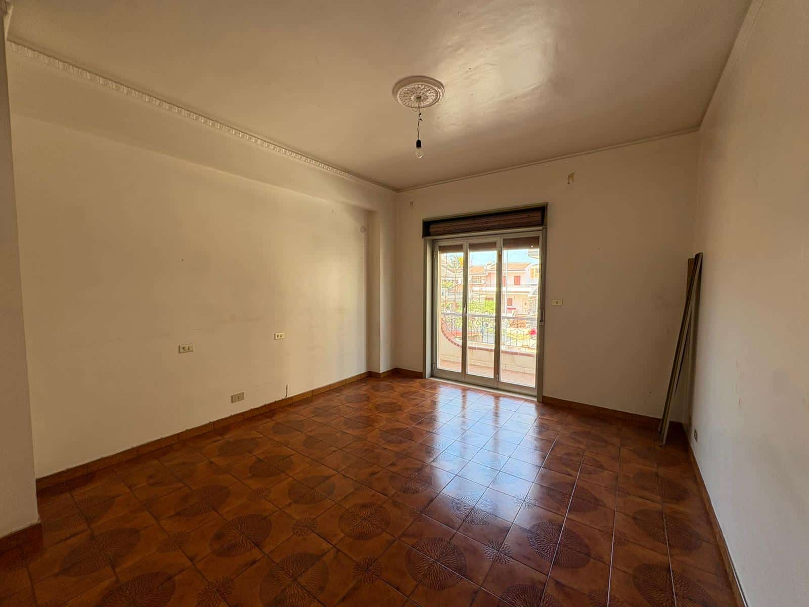 Interno di un appartamento vuoto con pareti bianche, pavimento in ceramica e grande finestra con balcone a Merì.