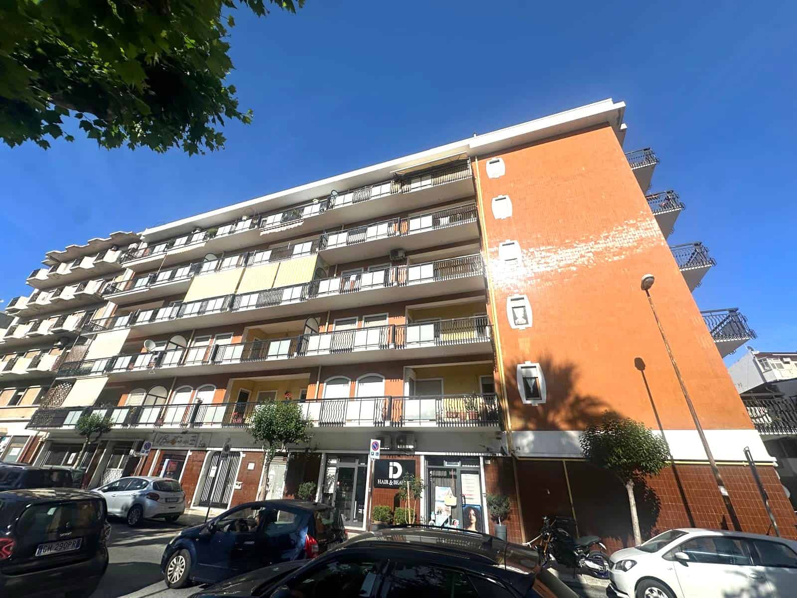Edificio residenziale moderno con balconi e parcheggio, vista frontale, in zona urbana.