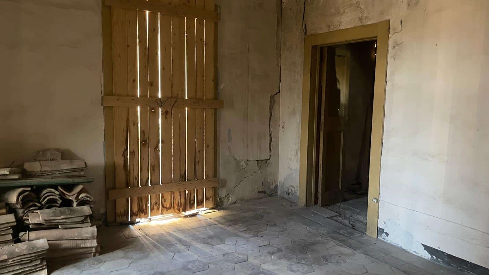 Immagine di un interno di una casa rustica in fase di ristrutturazione, con pareti in pietra, pavimento in piastrelle e porta in legno, pronta per lavori di restauro.