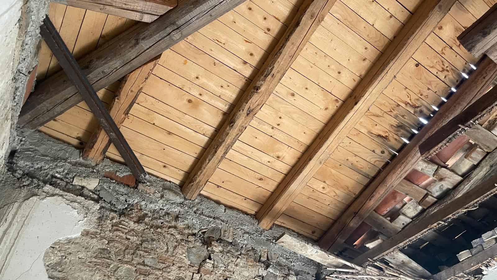 Tetto in legno con travi a vista in un ambiente rustico, mostra dettagli di costruzione e materiali naturali.