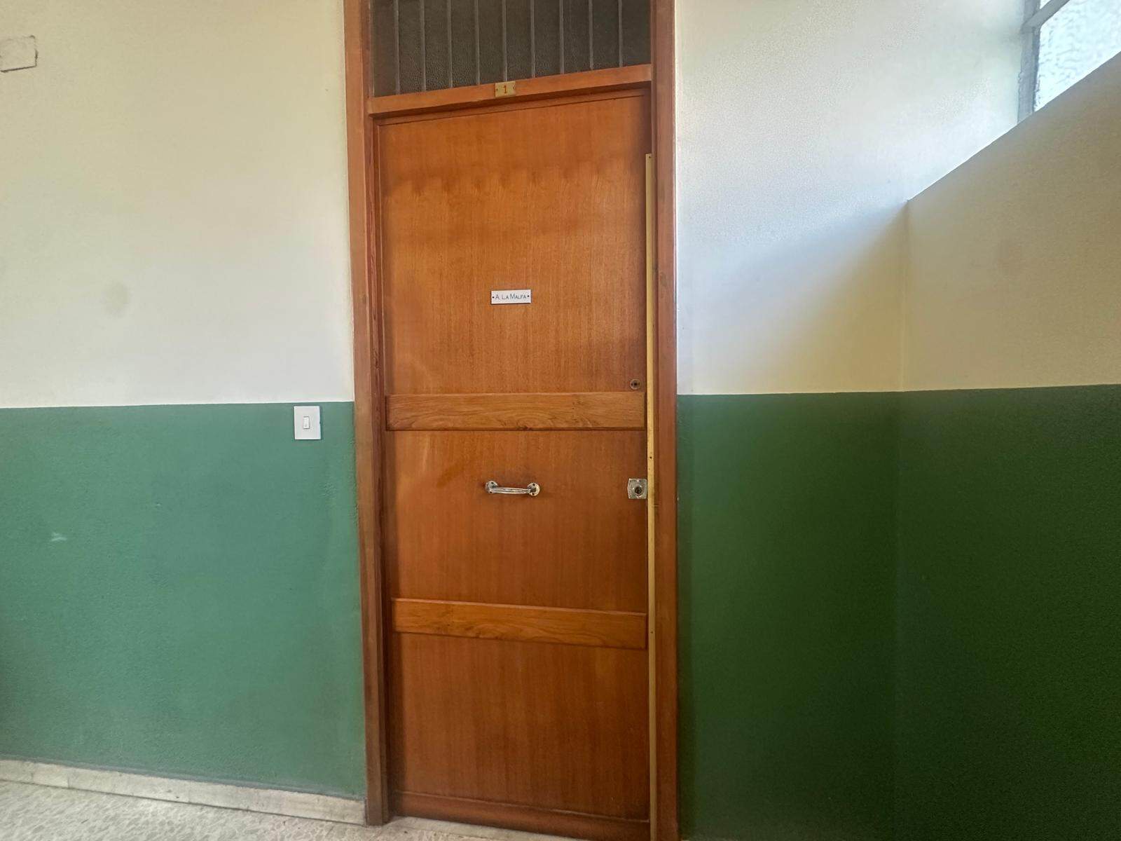 Porte in legno con maniglia e finestra in vetro, situate in un ambiente interno con pareti dipinte in verde e bianco, illuminato dalla luce naturale.
