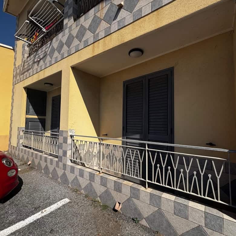 Balcone di un appartamento in vendita a Spadafora, con ringhiera in metallo e persiane nere, facciata gialla e dettagli in piastrelle.