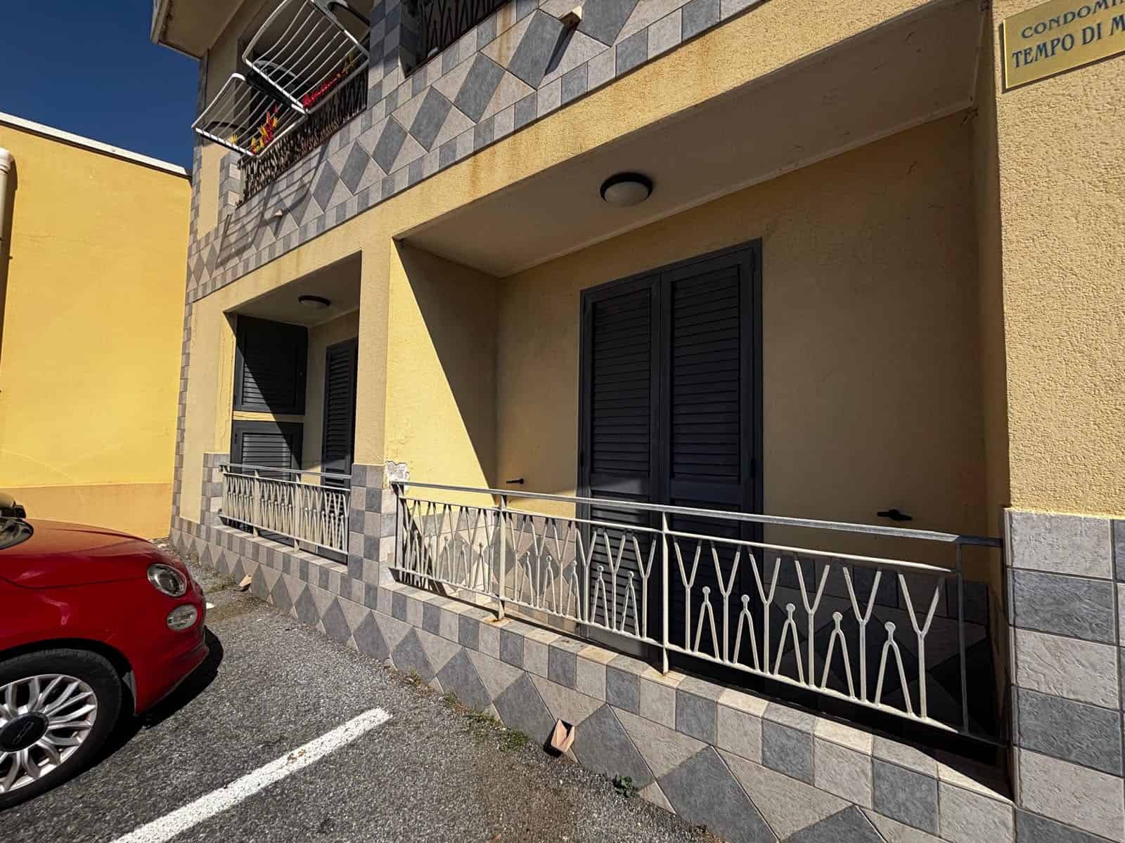 Balcone di un appartamento in vendita a Spadafora, con ringhiera in metallo e persiane nere, facciata gialla e dettagli in piastrelle.