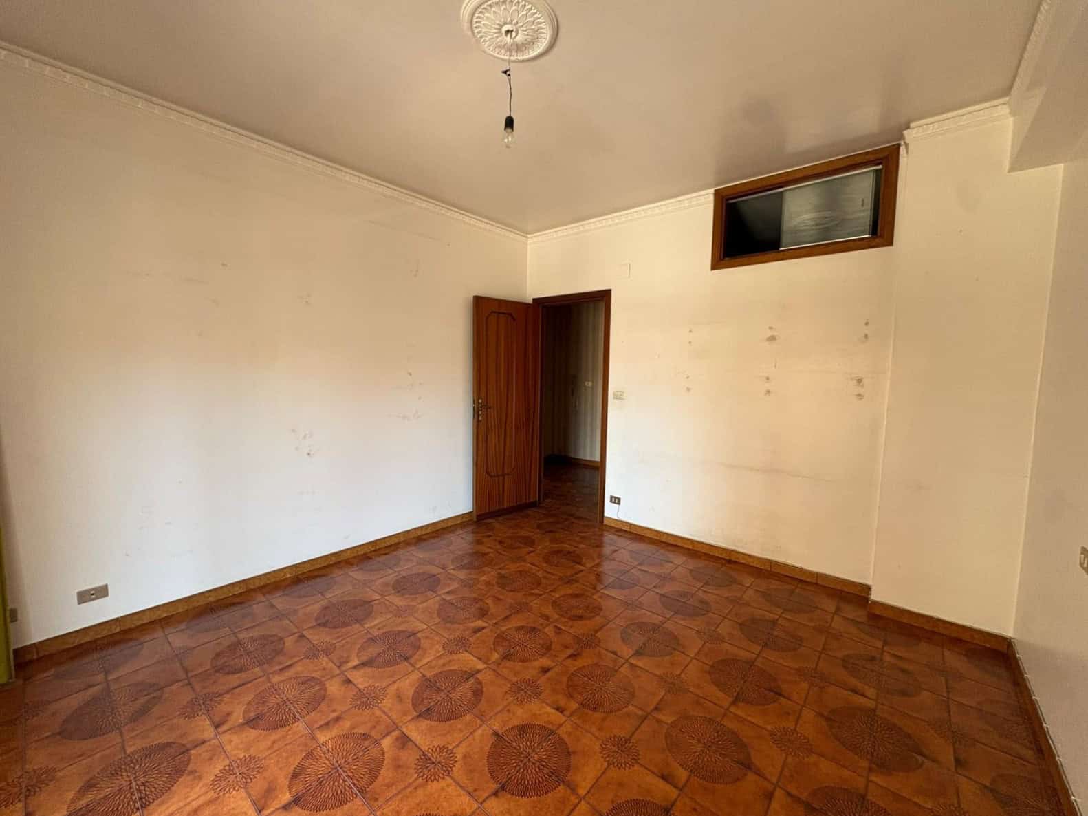 Interno di un appartamento in vendita a Merì, con pareti bianche e pavimento in piastrelle di ceramica marroni.