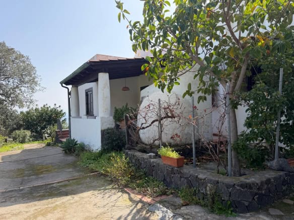 Un'abitazione rustica con pareti bianche, tetto in tegole e giardino con piante e alberi, immersa in un ambiente naturale e tranquillo, ideale per una casa di campagna o una seconda casa in campagna.