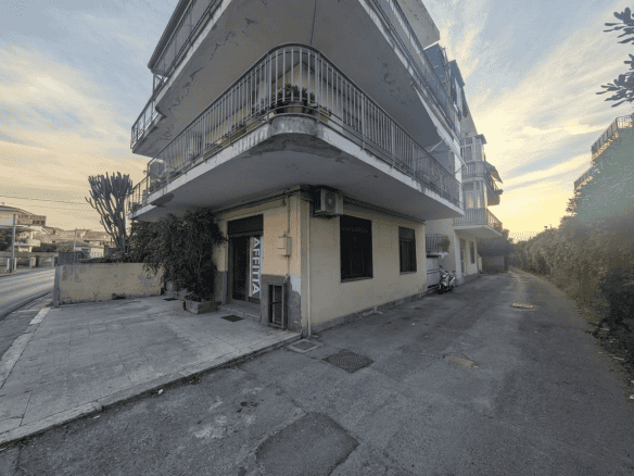 Edificio residenziale con balconi e negozio al piano terra, vista da strada in zona urbana.