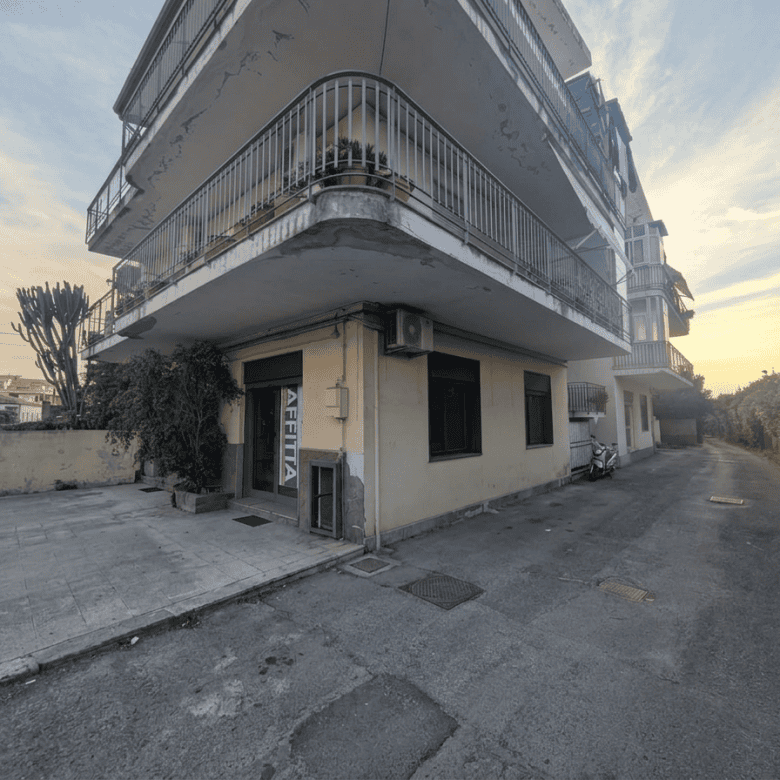 Edificio residenziale con balconi e negozio al piano terra, vista da strada in zona urbana.