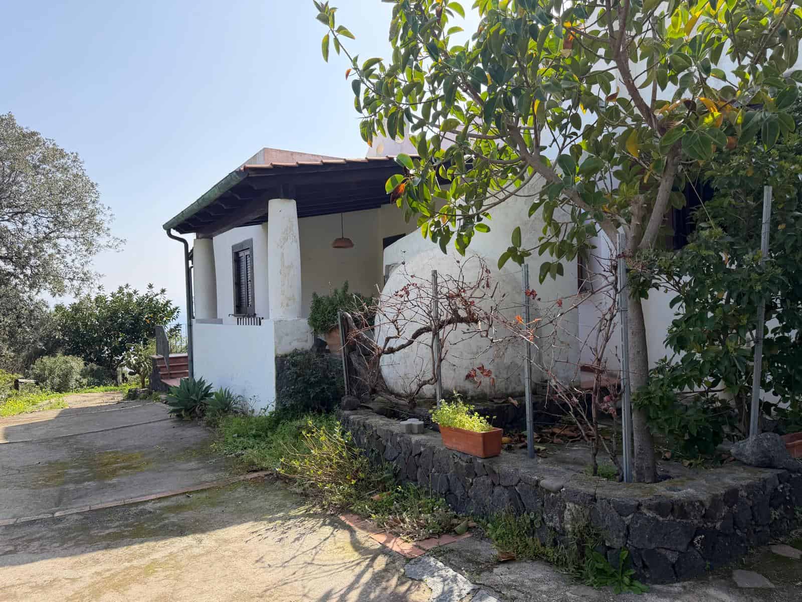 Un'abitazione rustica con pareti bianche, tetto in tegole e giardino con piante e alberi, immersa in un ambiente naturale e tranquillo, ideale per una casa di campagna o una seconda casa in campagna.