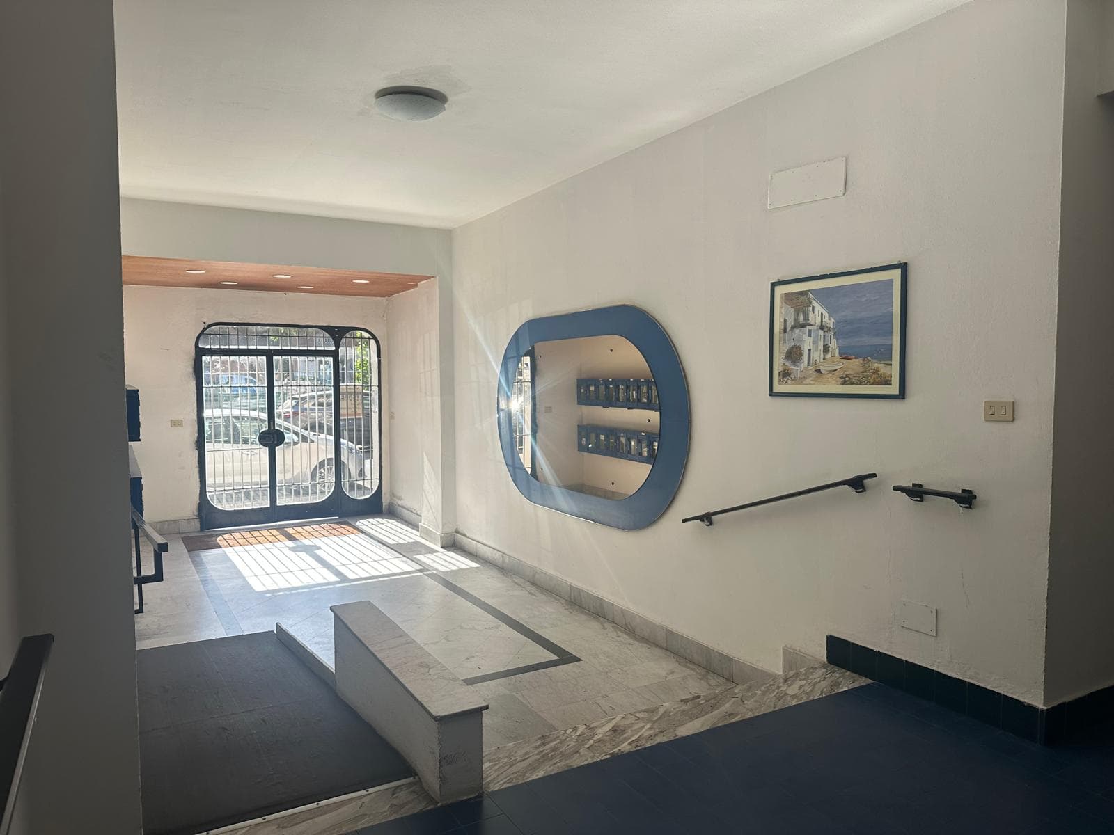 Interno di un ingresso moderno con pareti bianche, decorazioni minimaliste e porta d'ingresso in vetro con metallo, ideale per appartamenti e case in vendita o affitto a NextCasa.