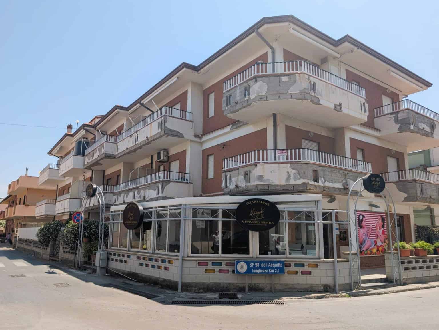 Edificio residenziale con negozio al piano terra, balconi e facciata in mattoni rossi, situato in zona urbana soleggiata e ben servita.