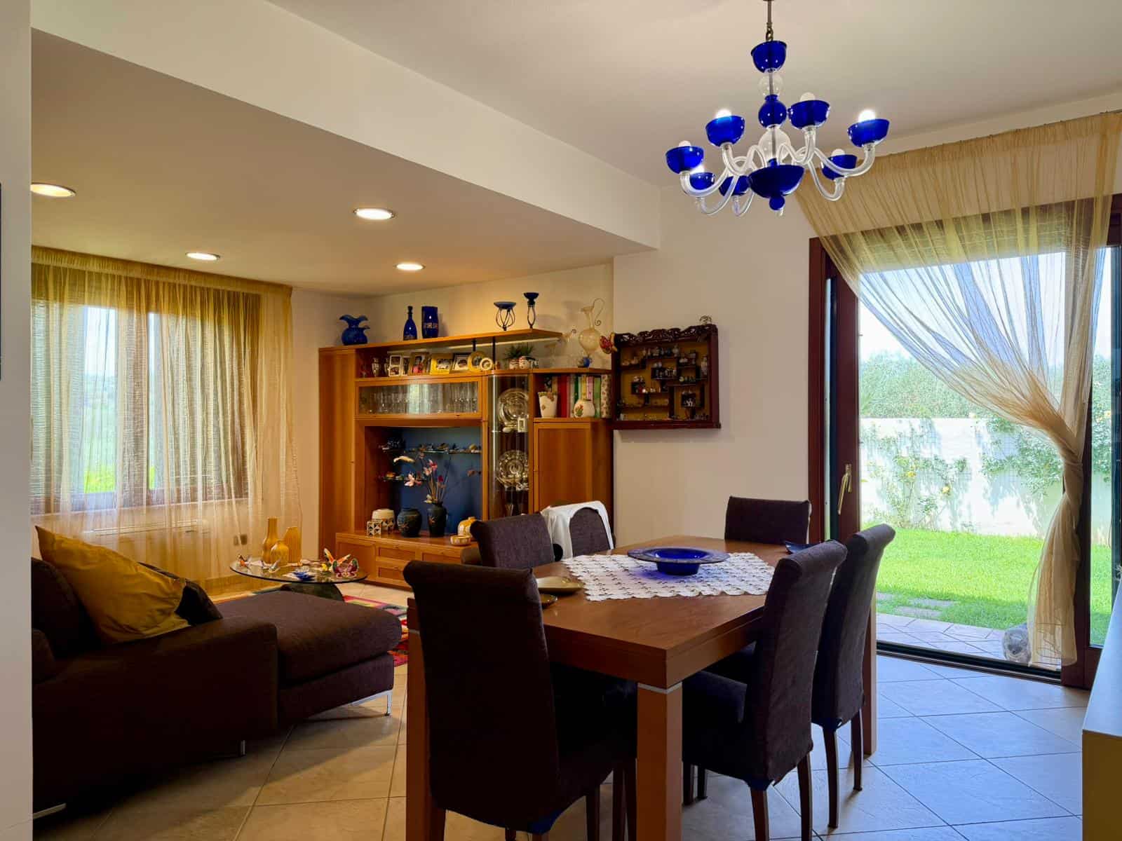 Interno di una villa con soggiorno e sala da pranzo, grande finestra con vista sul giardino.