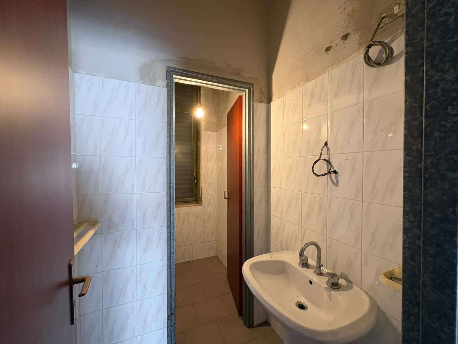 Bagno in fase di ristrutturazione con pareti in piastrelle bianche e lavabo con rubinetto.