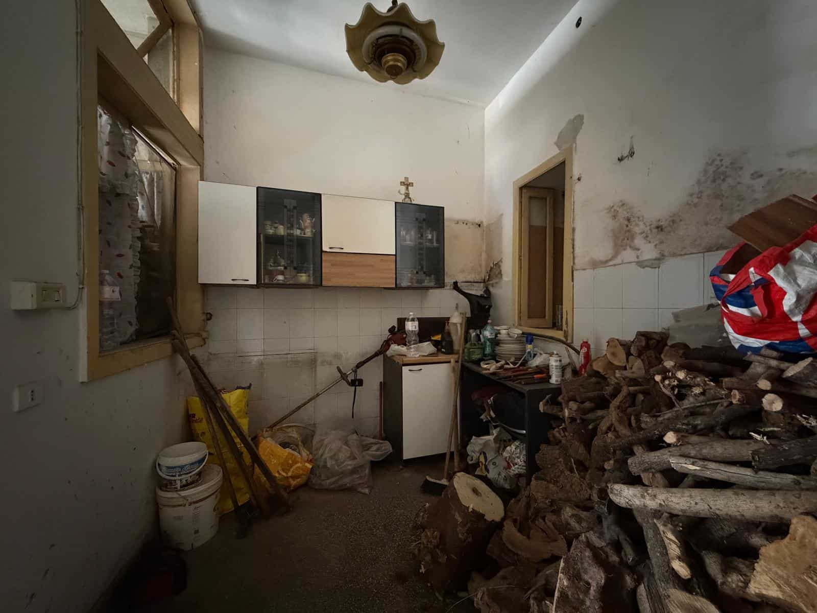 Interno di una casa in stato di abbandono con mobili rotti e detriti sul pavimento.