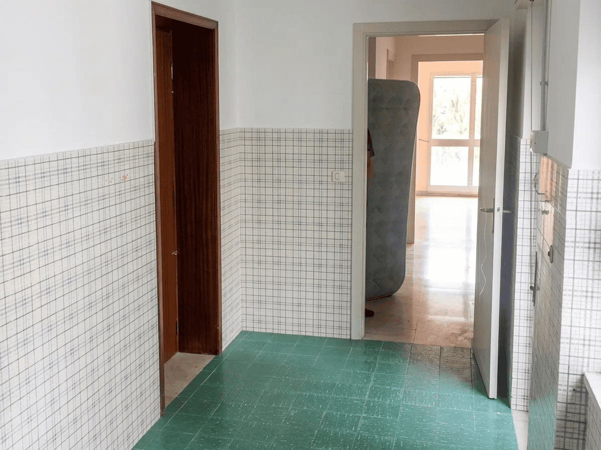 Interno di un appartamento con pareti rivestite in piastrelle colorate e porta aperta che conduce a una stanza luminosa con finestra.