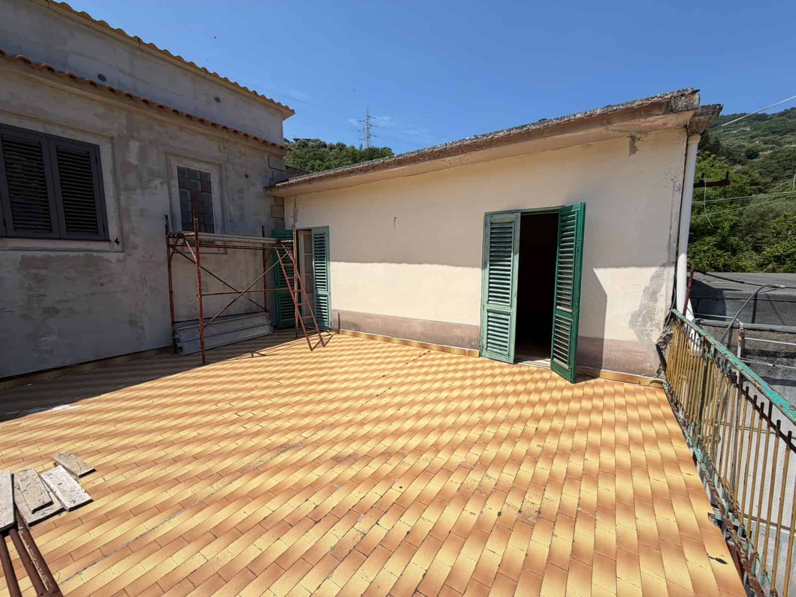 Terrazza panoramica con vista su case e natura, pavimentata con tegole in terracotta, in un contesto residenziale tranquillo e soleggiato.