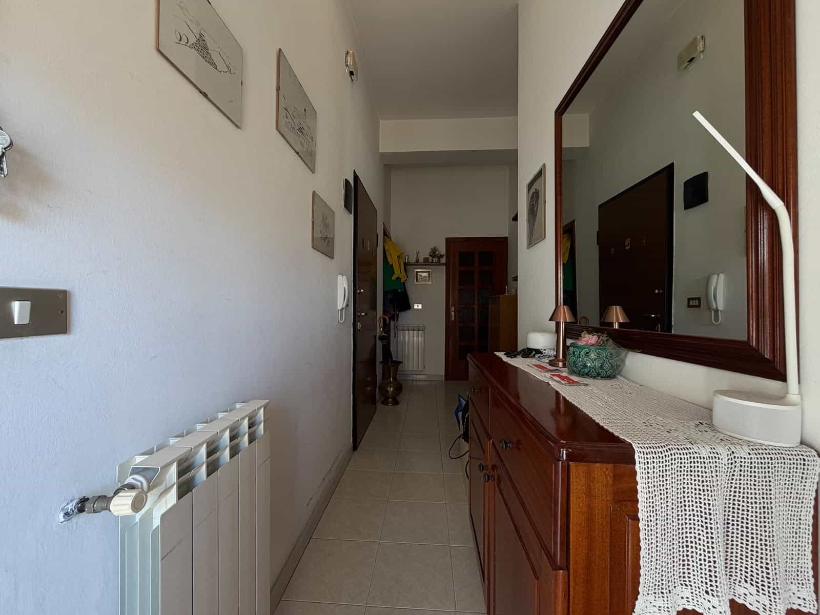 Ingresso di un appartamento con mobili in stile classico e decorazioni alle pareti, vista verso il corridoio e la porta d'ingresso.