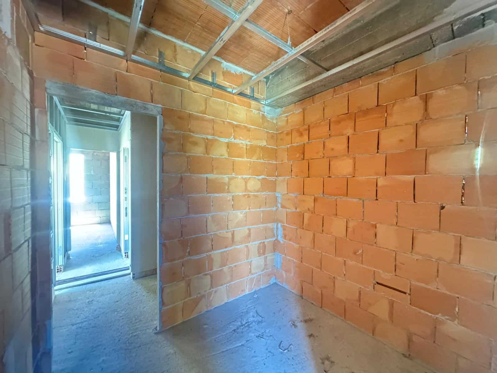 Interno di un edificio in costruzione con pareti in mattoni e struttura in metallo visibile sul soffitto.