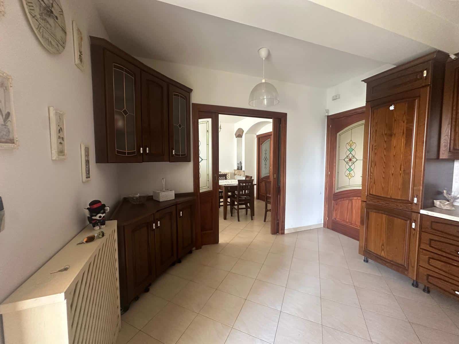 Interno di un appartamento con mobili in legno e porta d'ingresso in legno con vetrata decorativa, vista sulla sala da pranzo.