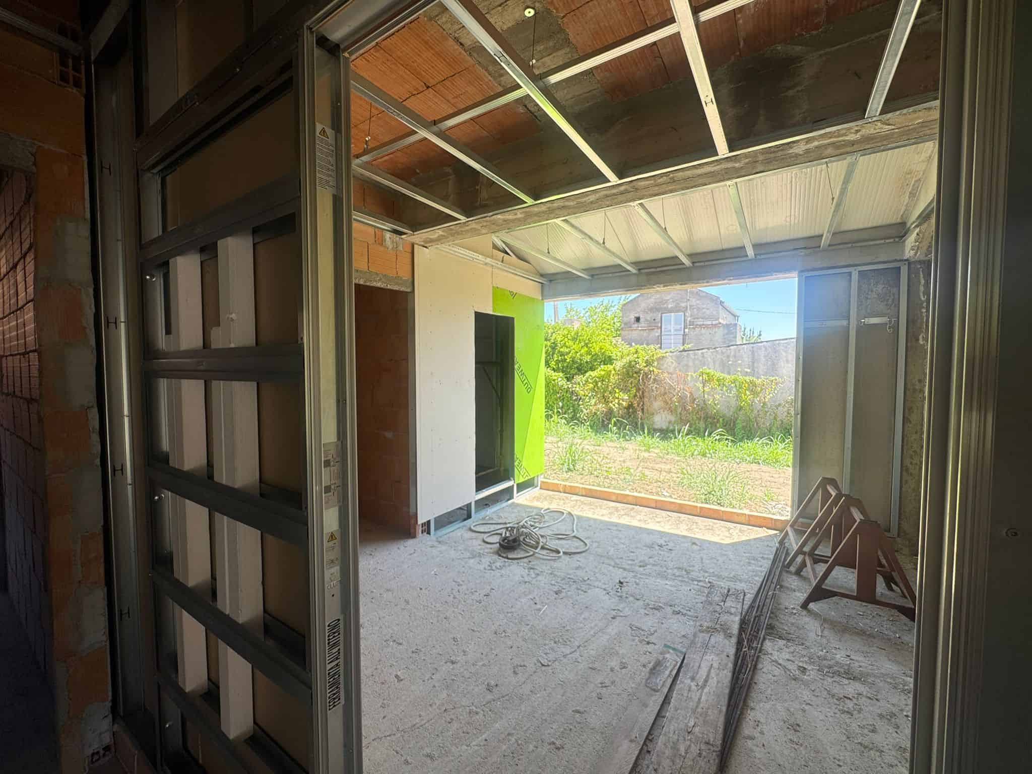 Interno di un appartamento in costruzione con vista su giardino esterno, struttura in fase di completamento.