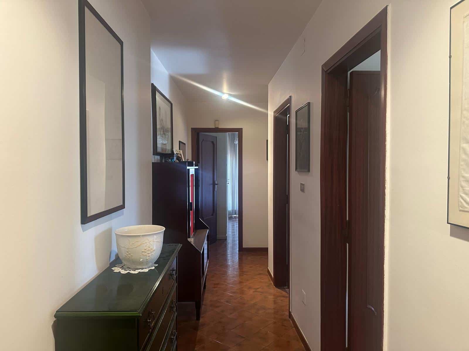 Porte interne in legno scuro in un appartamento moderno con pareti bianche e decorazioni artistiche, corridoio luminoso con pavimento in parquet, arredamento elegante e accogliente.