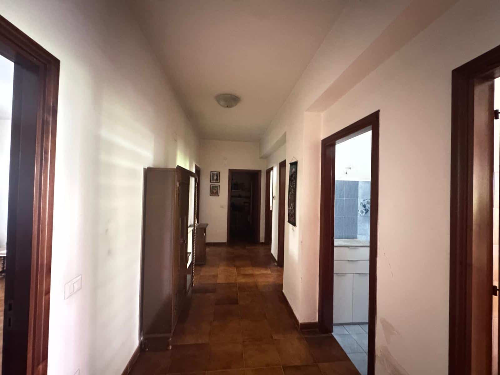 Corridoio interno di un appartamento con pareti bianche, pavimento in legno e porte in legno scuro, ambiente luminoso e accogliente, ideale per case in vendita o affitto.