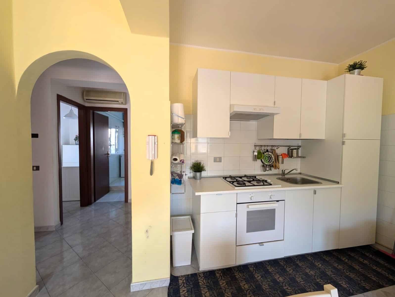 Cucina moderna con mobili bianchi e piano cottura a gas in un appartamento luminoso, con pareti gialle e dettagli decorativi.