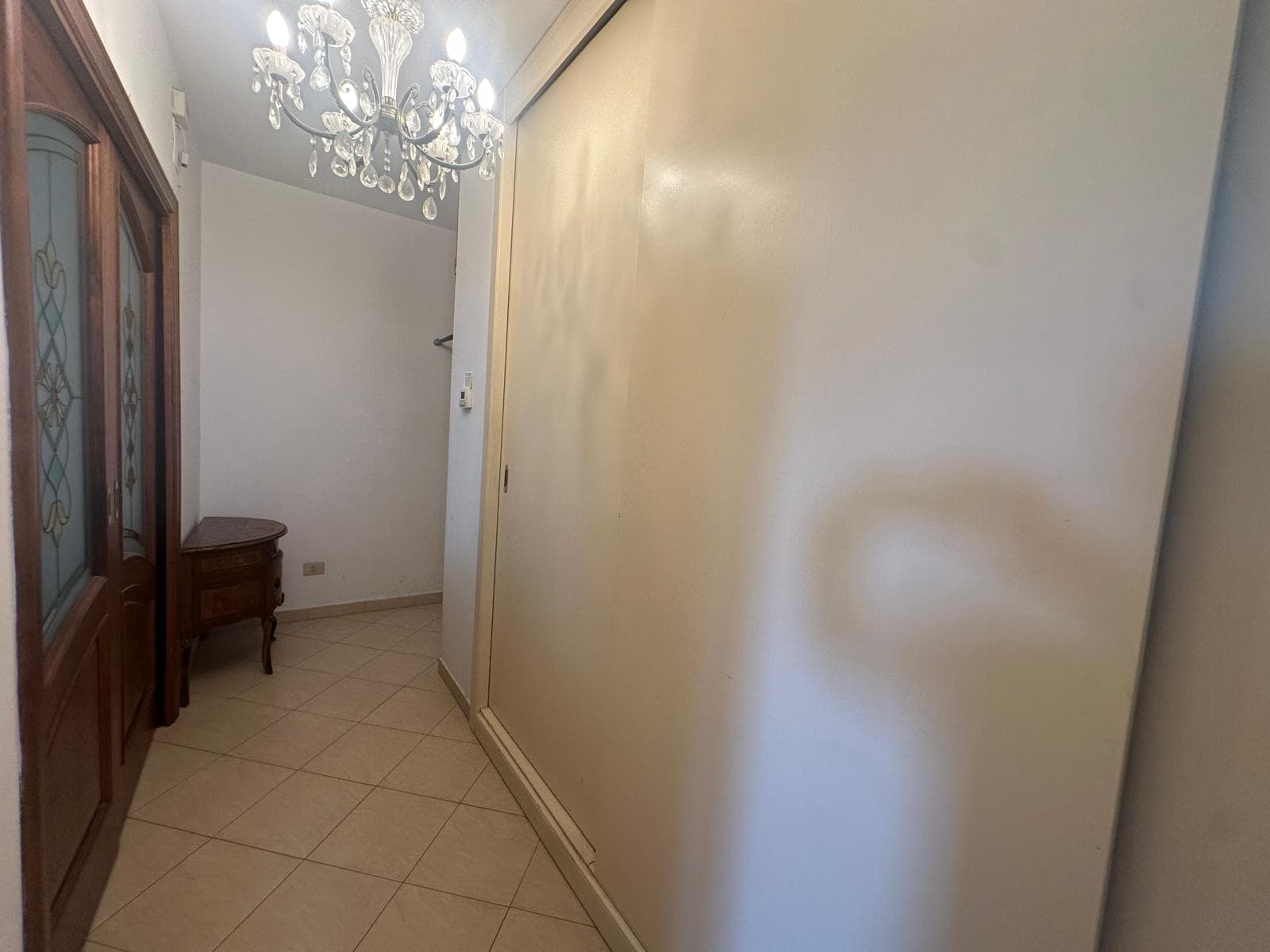 Ingresso di un appartamento con pareti beige, pavimento in piastrelle e lampadario elegante.