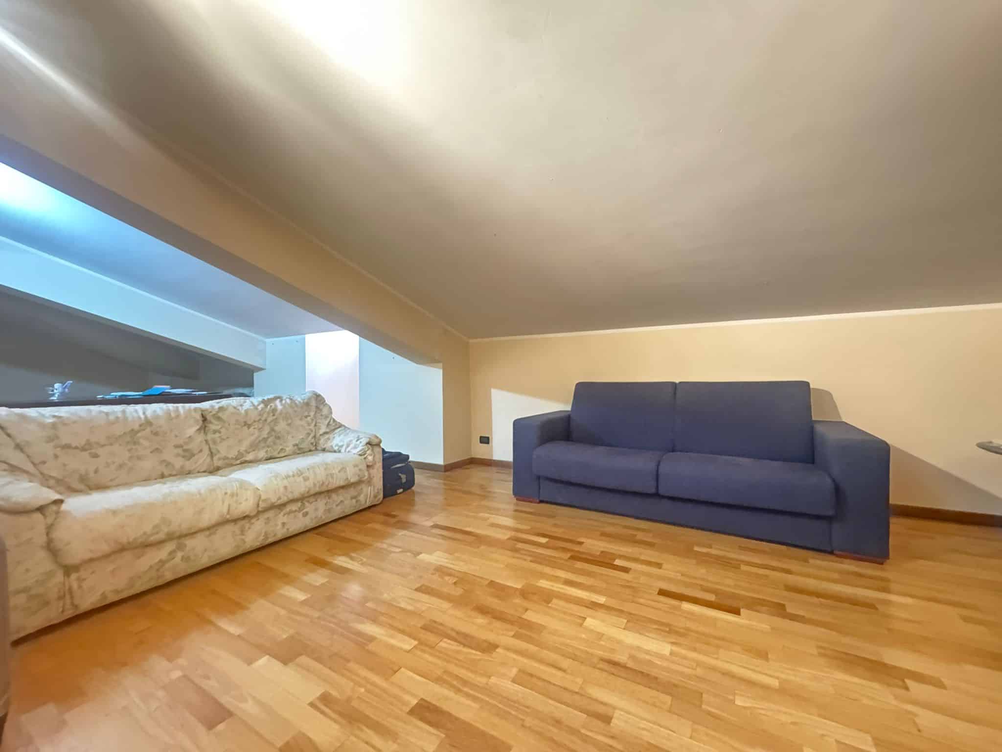 Ampio soggiorno mansardato con due divani, uno beige e uno blu, e pavimento in parquet, in via San Vito, Barcellona P.G.