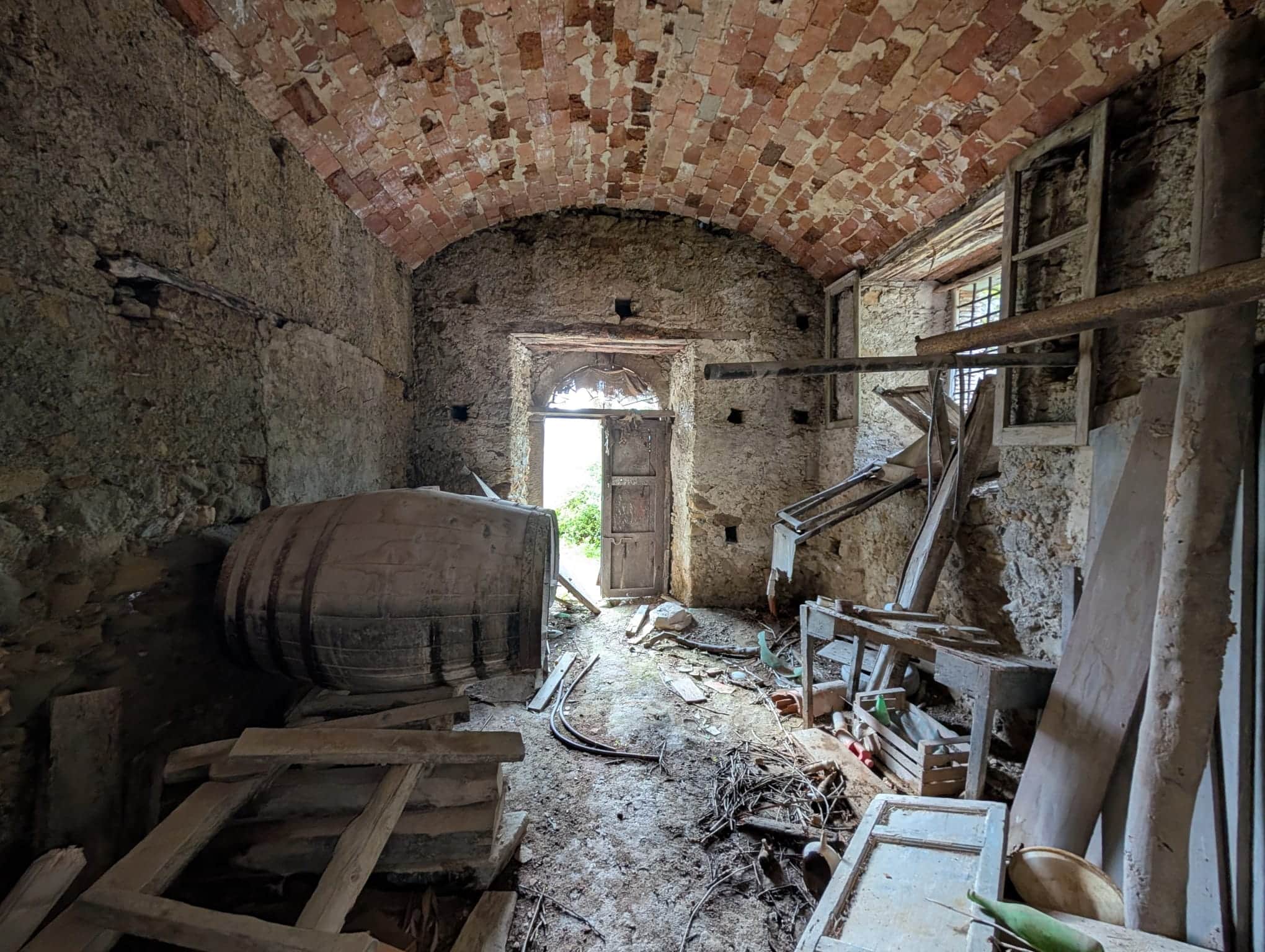 Interno di un rudere in vendita a Patti, con pareti in pietra e soffitto a volta in mattoni, in condizioni di abbandono e con materiali di recupero.