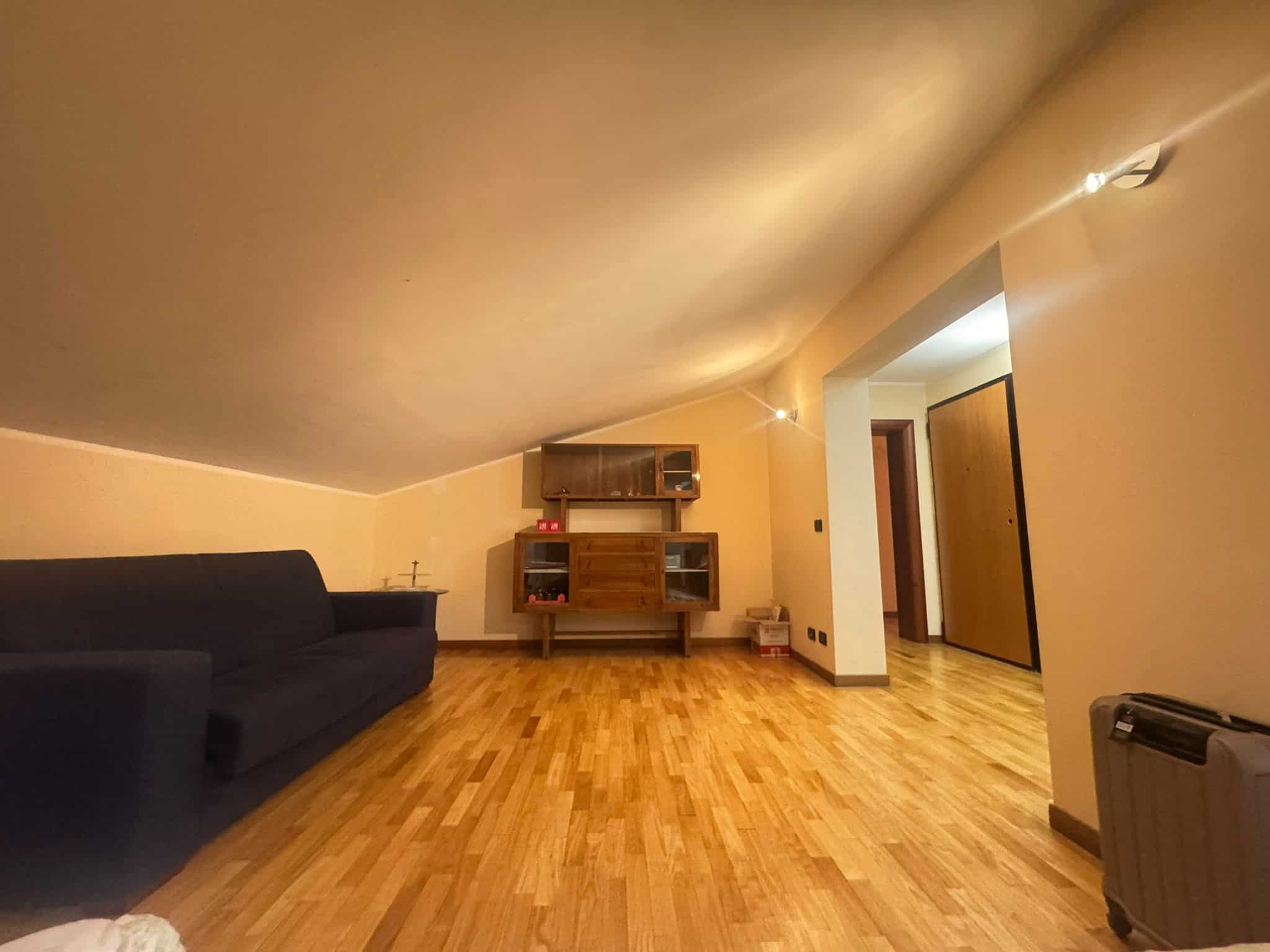 Ampio soggiorno mansardato con pavimento in parquet, divano nero e mobile porta TV in legno, in vendita in via San Vito, Barcellona P.G.