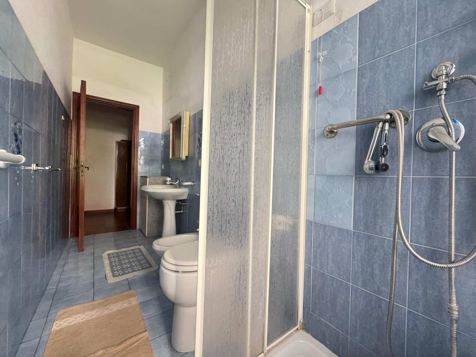 Lavabo e servizi igienici in bagno con piastrelle blu, doccia con parete in vetro, accessori moderni e ambiente luminoso, ideale per ristrutturazioni e soluzioni abitative di qualità.