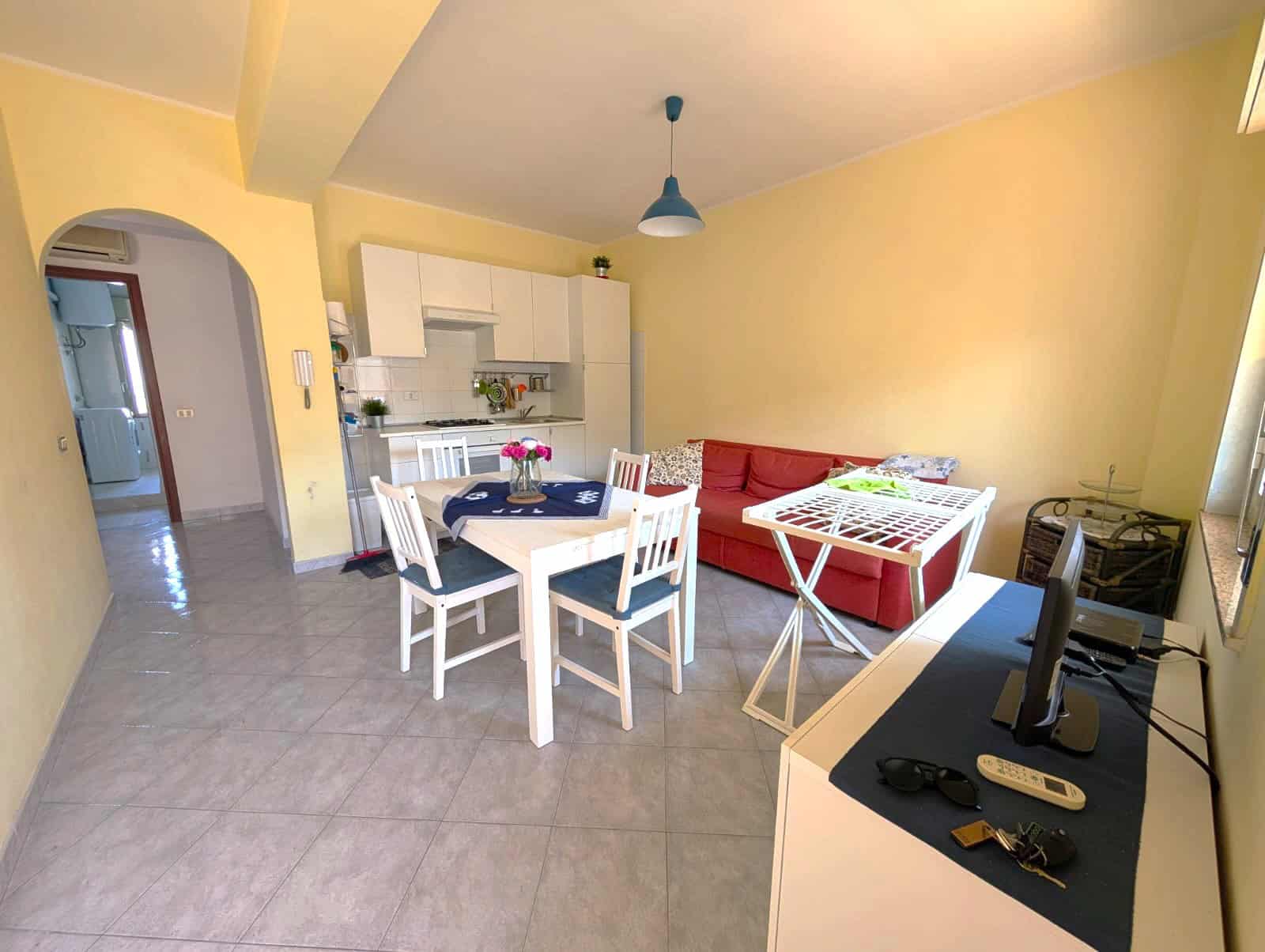 Soggiorno luminoso con cucina open space, tavolo da pranzo, divano rosso e area relax, arredamento funzionale e accogliente, ideale per vivere in comfort.