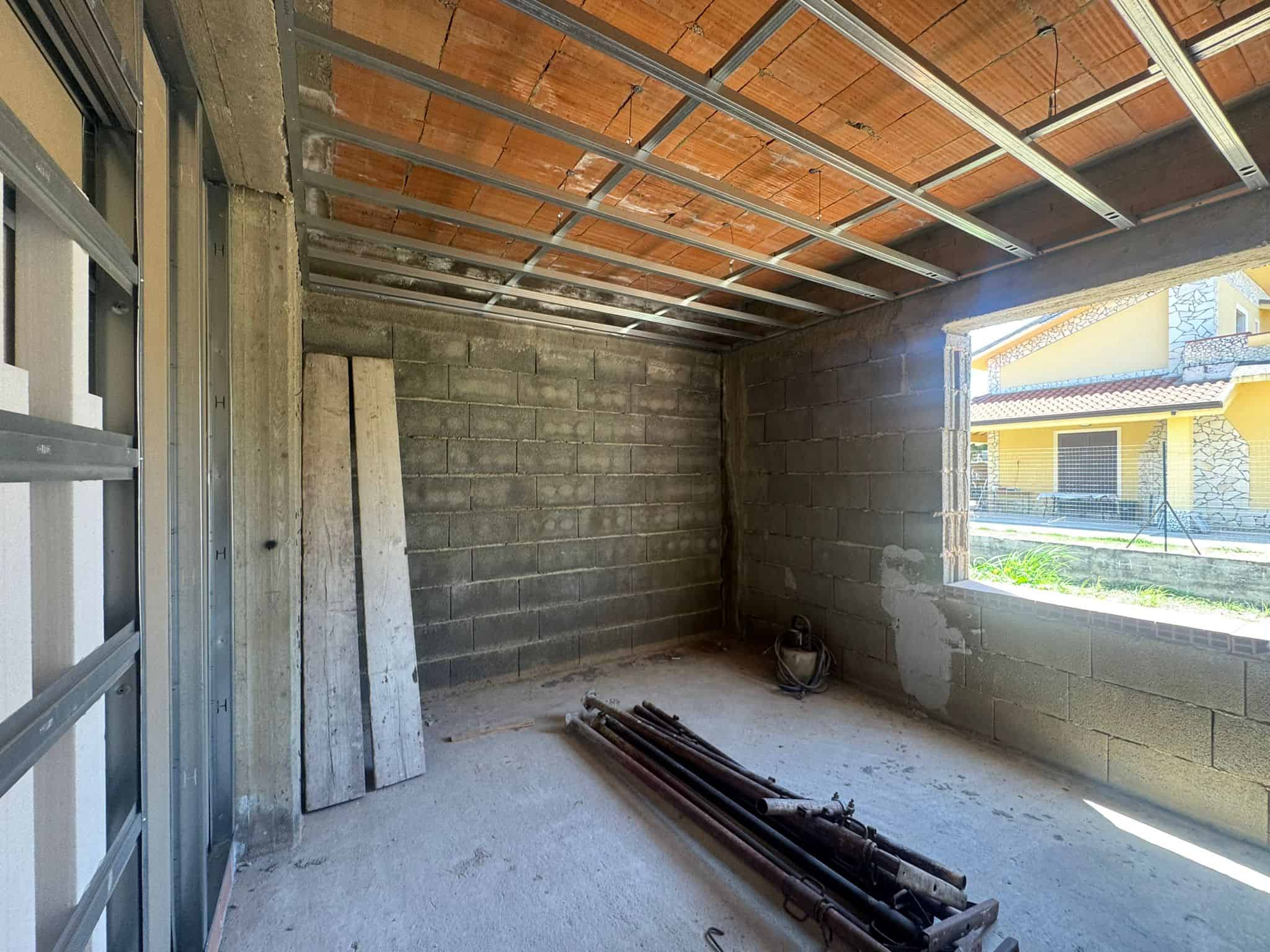 Interno di una stanza in costruzione con pareti in cemento e soffitto con struttura metallica.