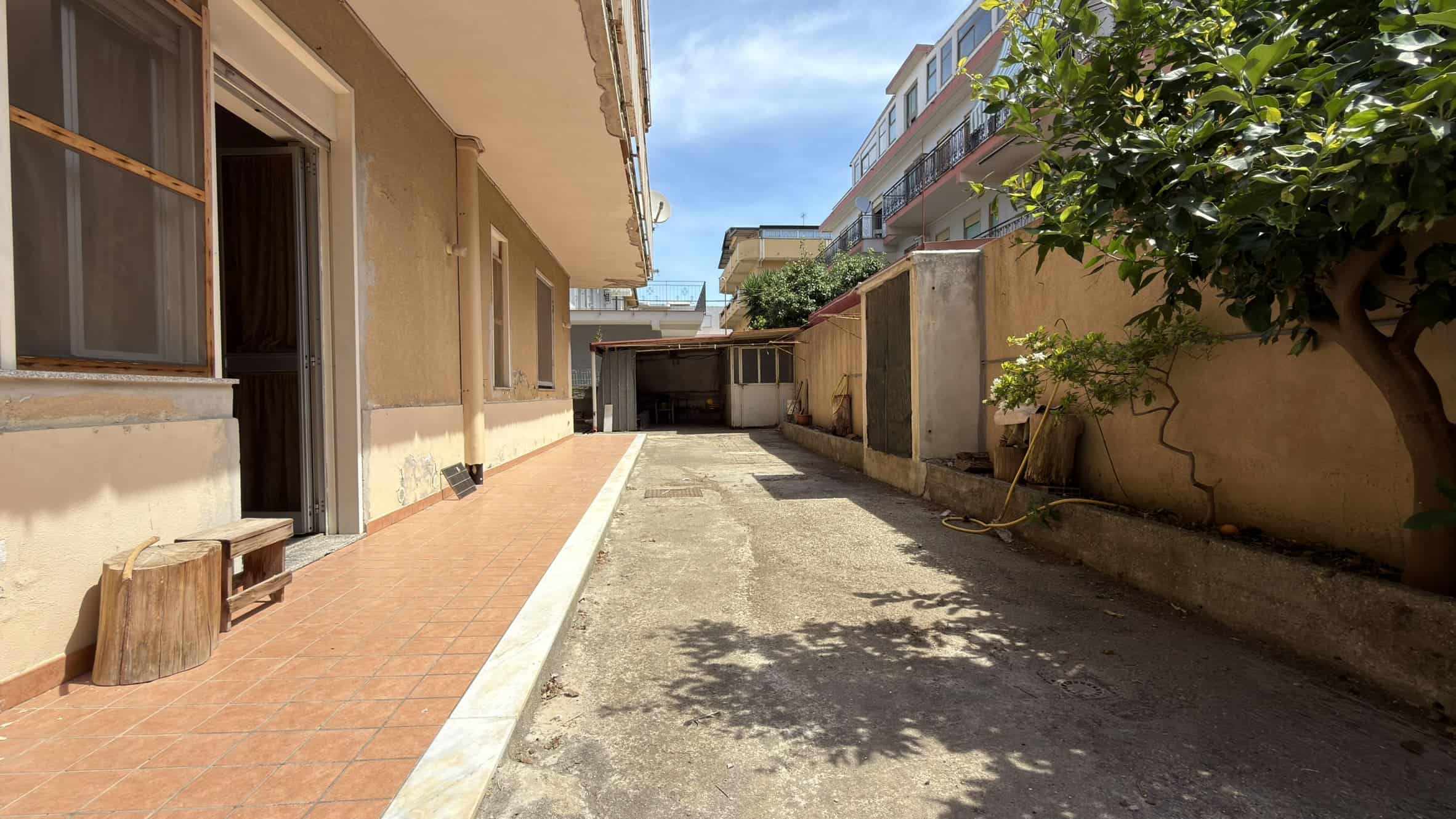 Spazio esterno di un appartamento con cortile privato, pavimentato e con alberi, in zona residenziale.