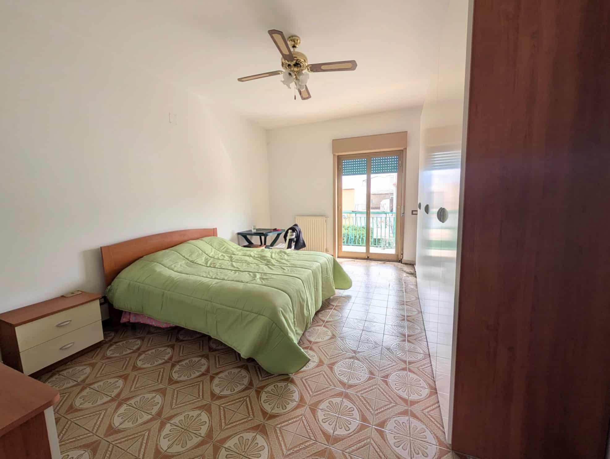 Camera che mostra una camera da letto con letto matrimoniale, armadio, e balcone con vista esterna.