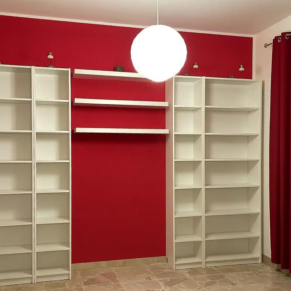 Scaffale bianco in soggiorno con parete rossa e lampada a soffitto, arredamento moderno e funzionale.