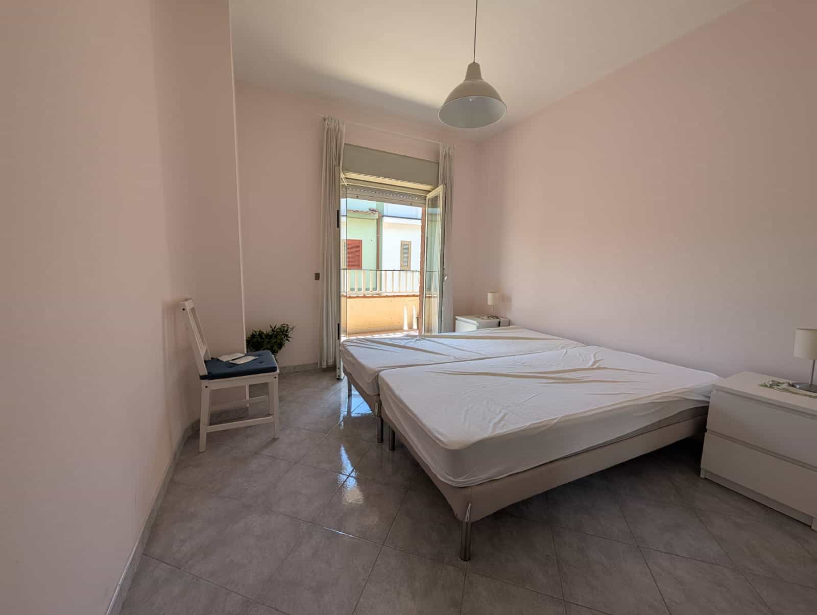 Letto matrimoniale in camera luminosa con vista su balcone, arredamento semplice e moderno, pavimento in marmo, ideale per affitti turistici o residenziali, NextCasa.
