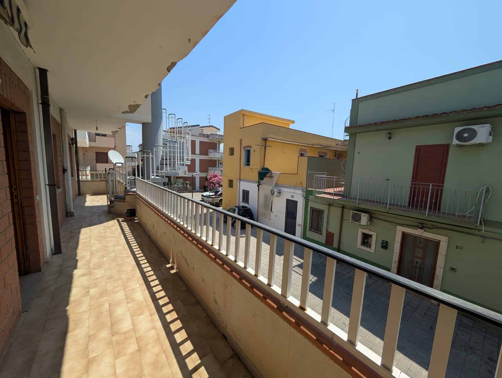 Ampia terrazza con vista su edifici residenziali colorati e cielo sereno, ideale per relax e socializzazione, situata in un quartiere tranquillo e ben servito.