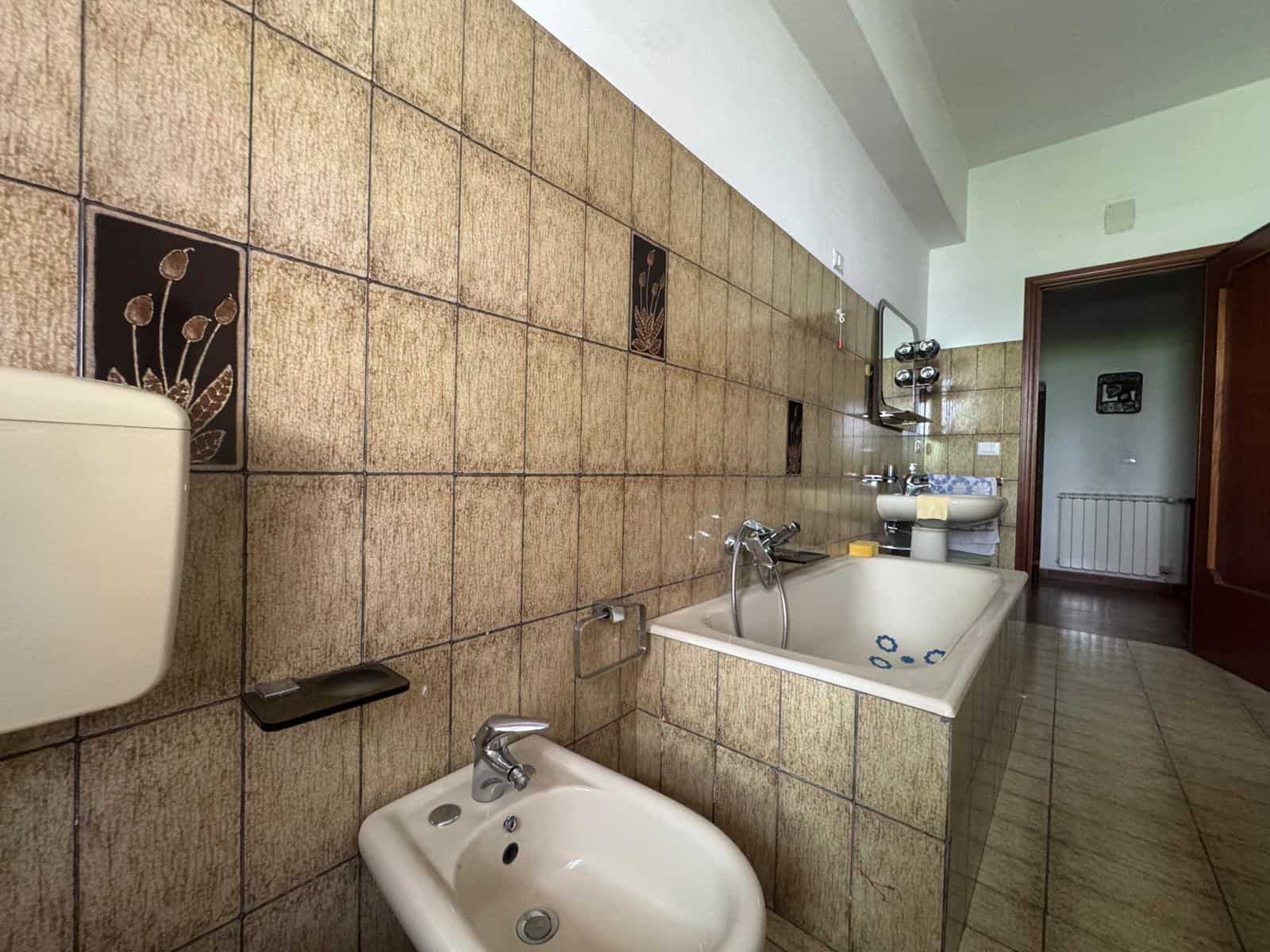 Lavandino e bidet in bagno con pareti rivestite di piastrelle marroni e decorazioni floreali, ambiente spazioso e luminoso, ideale per ristrutturazioni e miglioramenti domestici.