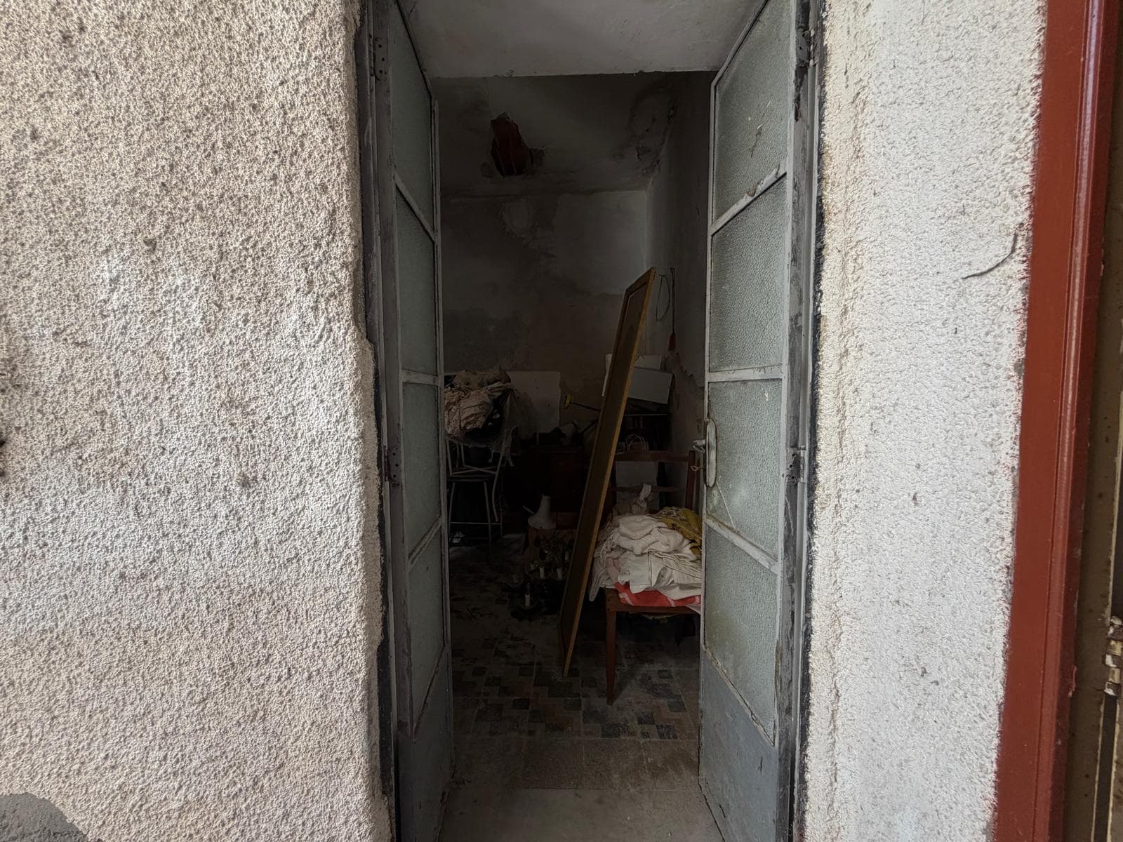 Ingresso di una casa in stato di abbandono con porte di metallo aperte e interno disordinato.