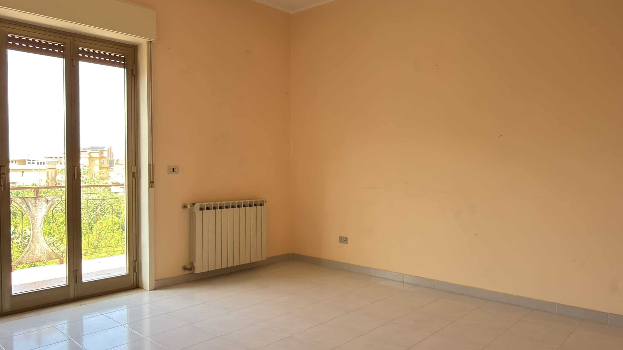 Stanza vuota con pareti beige, porta finestra e balcone, ideale per arredamento e ristrutturazioni immobiliari.