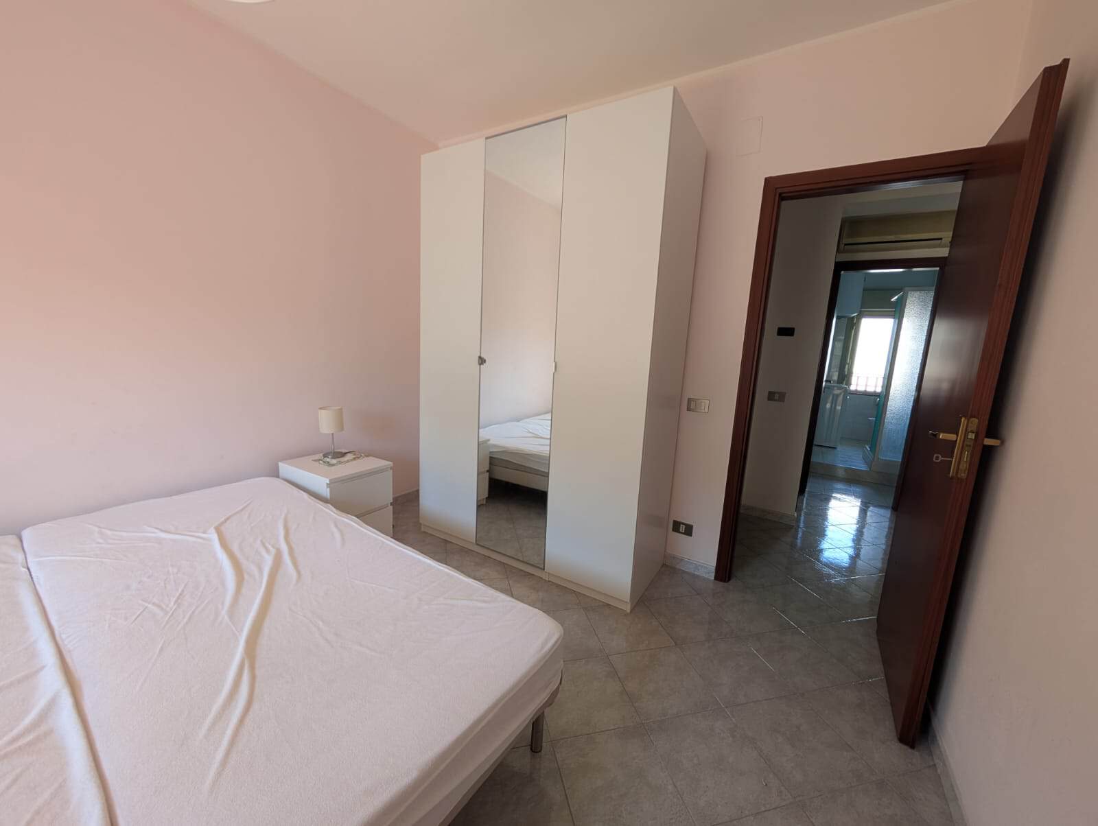Ampia camera da letto con letto matrimoniale, armadio a specchio e porta aperta che conduce a un corridoio luminoso, ideale per affitti turistici o residenziali.