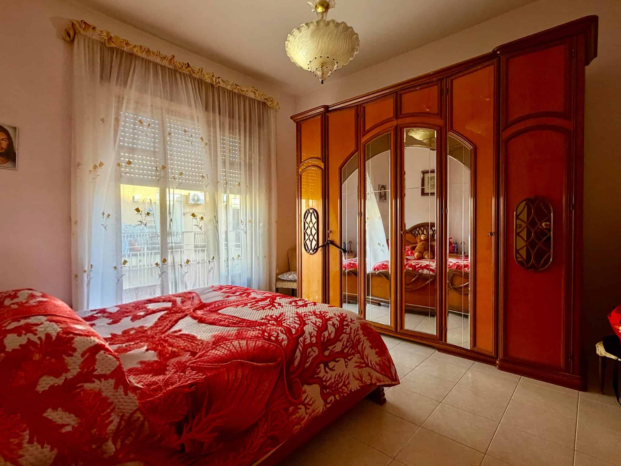 Camera che mostra una camera da letto con armadio in legno e letto con copriletto rosso.