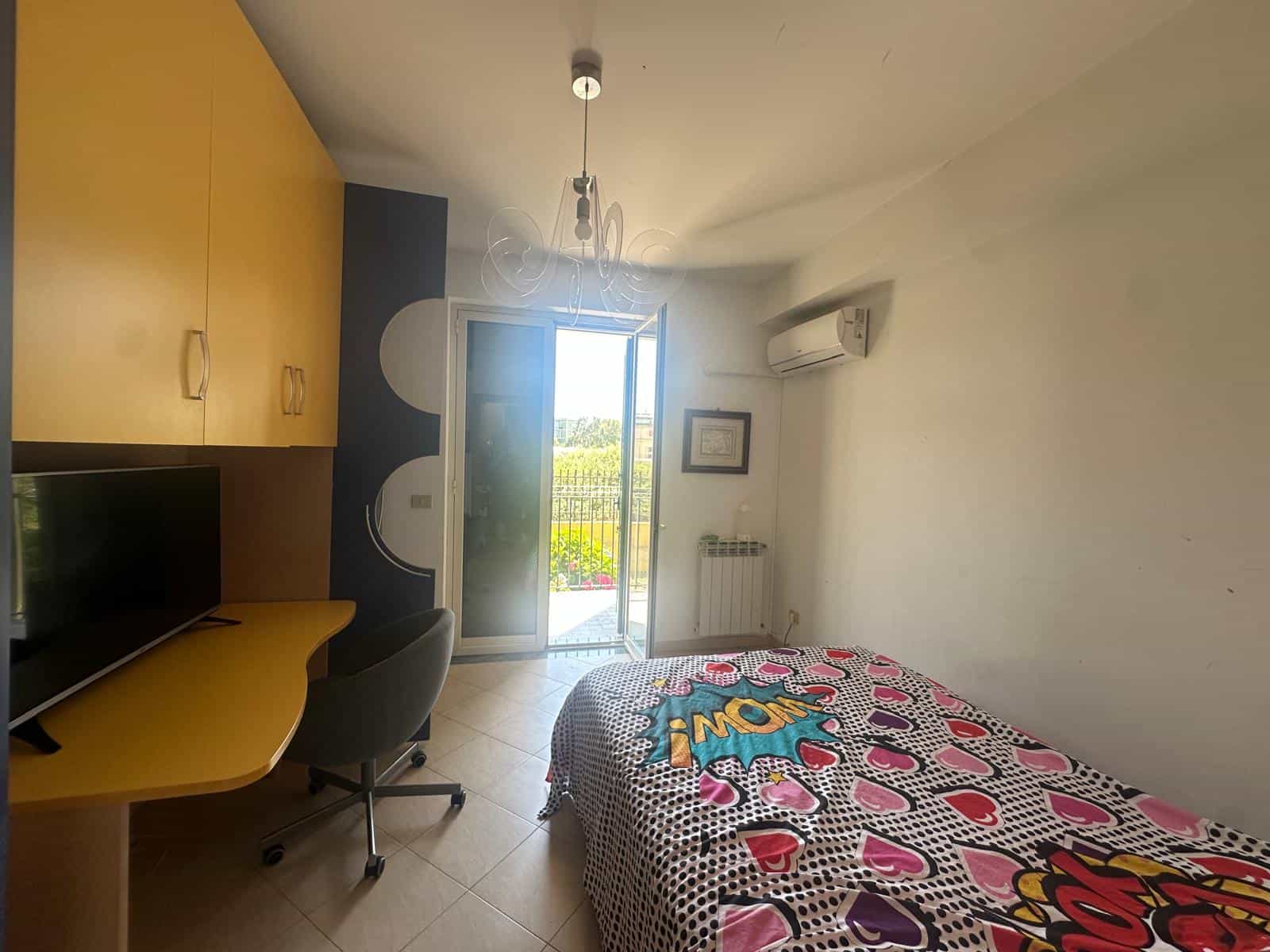 Interno di un appartamento con camera da letto, scrivania e balcone con vista.