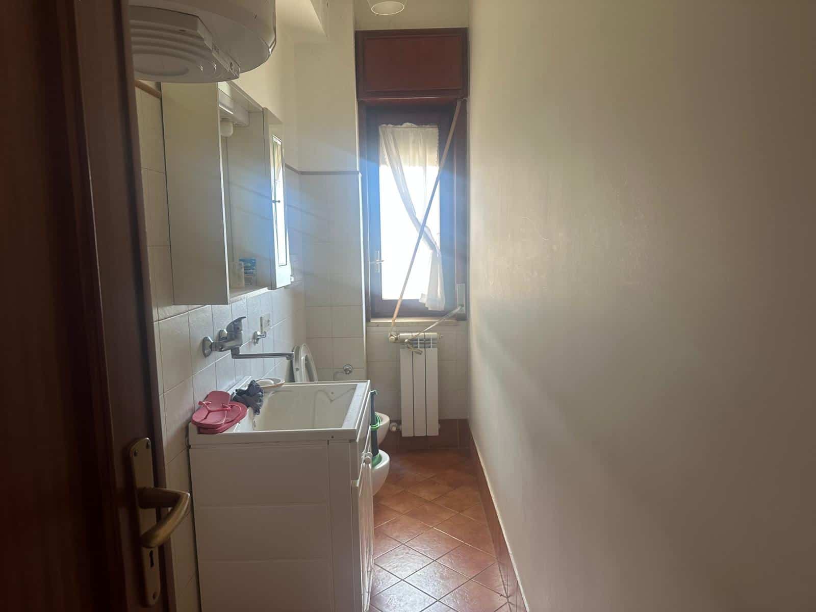 Lavanderia compatta con lavatrice, lavabo e finestra luminosa, ideale per spazi ridotti e pratici, in un appartamento moderno.