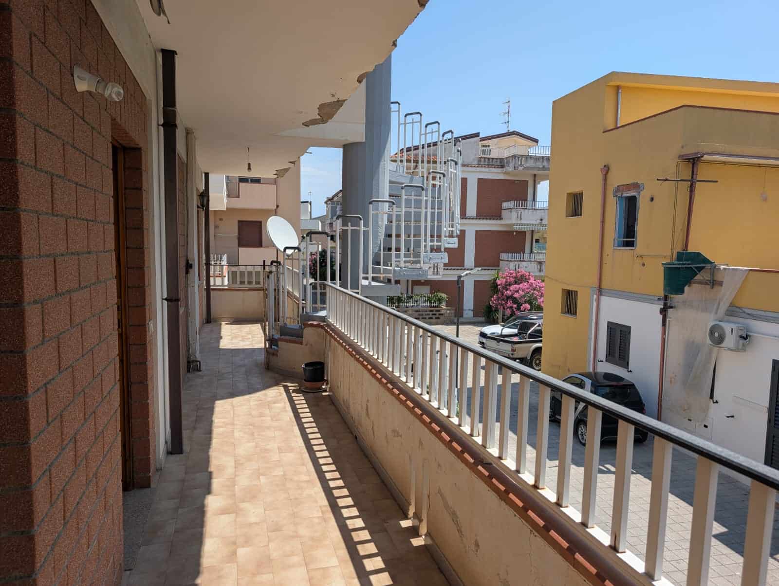 Ampio balcone con vista su quartiere residenziale, con piante e edifici colorati, ideale per relax e momenti all'aperto.