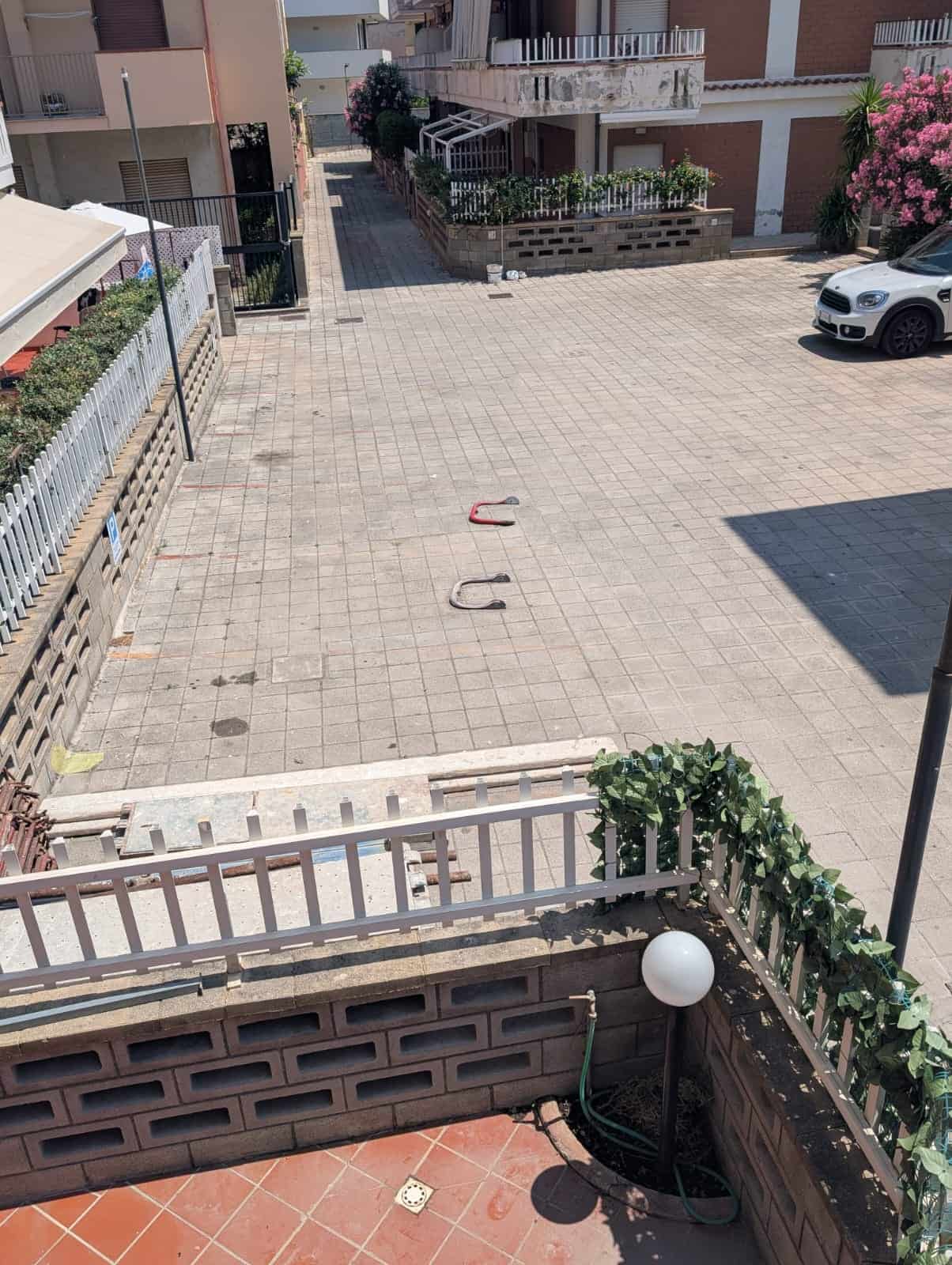Panchina e spazio di parcheggio in un cortile condominiale con auto e piante verdi, vista dall'alto di un'area esterna ben curata e spaziosa, ideale per relax e sosta veicoli.